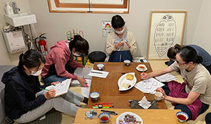 Women sit on a tatami mat and low table and write responses on handouts.