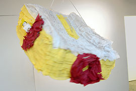 a photo of a piñata modeled after a dewalt travel-sized table saw made of yellow streamers for the sides, white streamers for the top, and red streamers for the knobs and miter gauge