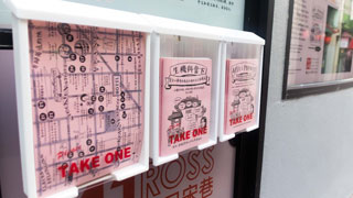A close-up photo of three outdoor brochure holders, holding maps and comic books on pink paper.