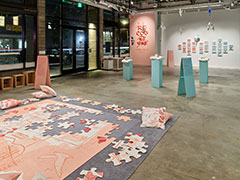 Installation view of gallery with a puzzle in the foreground, stuffed airplanes in the middle ground, and portraits in the background.