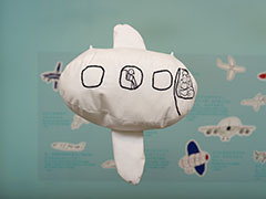 A stuffed airplane with a very round fuselage and stitching showing a pilot and child seated in a window.