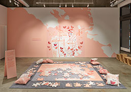installation view of a jumbo puzzle of a map of San Francisco, with a reference image on the wall