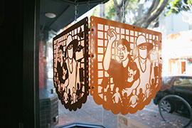 an lantern of steel with orange powdercoating showing a Latina next to a day laborer wearing a hat, surrounded by allies with linked arms