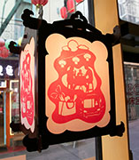 a wood lantern with red papercut depicting scenes in chinatown including a family eating at a night market