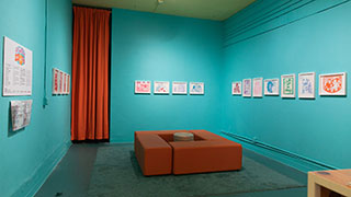 A wide shot of an exhibition of papercuts in a gallery with aqua-colored walls