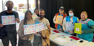 a group of participants holding up stamp collection sheets along side designers in a black box theater space