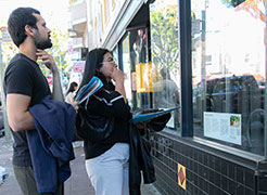 A man and woman stand outside a storefront viewing a lantern in the window.