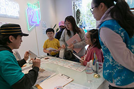 A family with young children speak with a person seated behind a desk, who holds up an envelope.