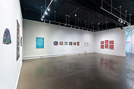 Another installation view of the gallery, with clusters of artworks in aqua blue, multi-color, and red and white.